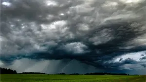 Dark, stormy clouds over a green field.